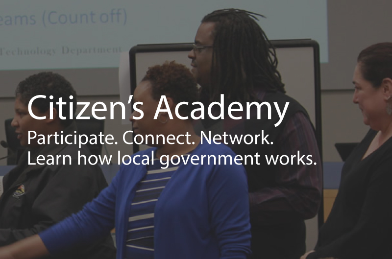 Photo showing a group of adults smiling, and participating in an activity together. Caption: Citizen's Academy. Participate. Connect. Network. Learn how local government works.